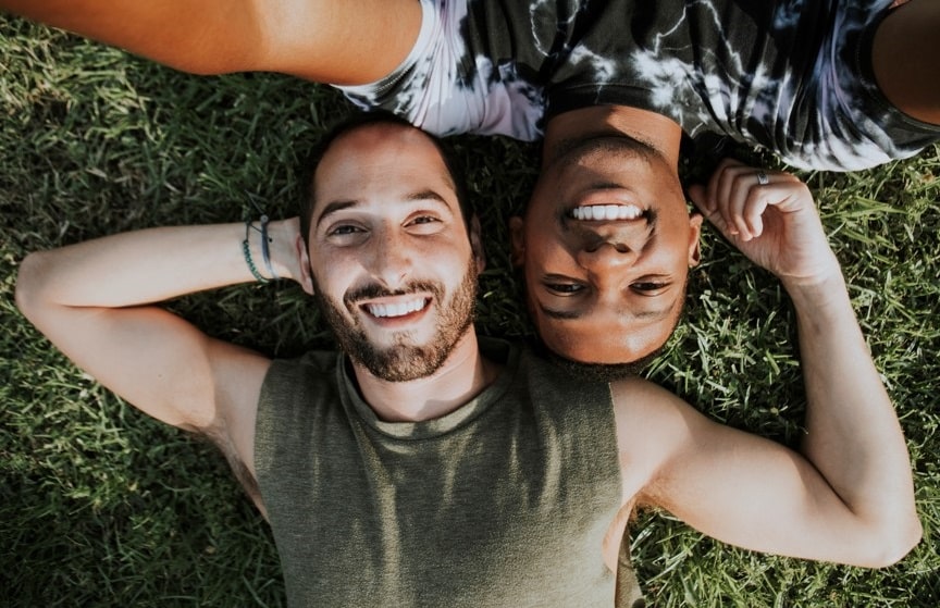 Gay Romance in der Natur mit einem schwarzen Mann und einem kaukasischen Mann, lächelnd auf grünem Gras liegend