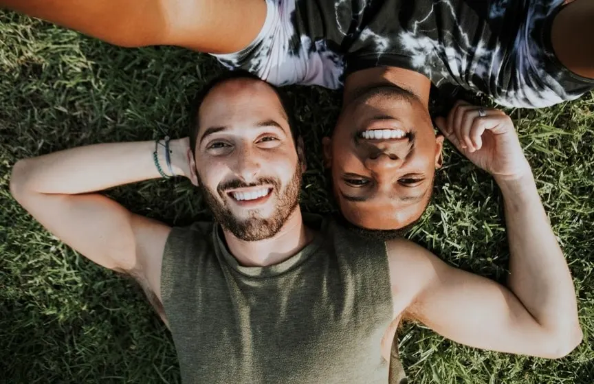 Gay romance in nature with a black man and a Caucasian man lying on green grass, smiling
