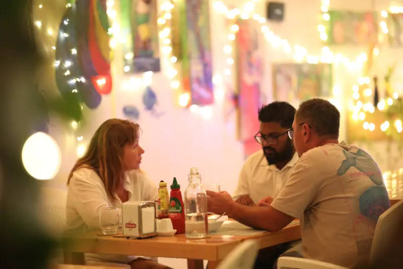 Conversation à trois autour d'une table de restaurant, lumière chaleureuse